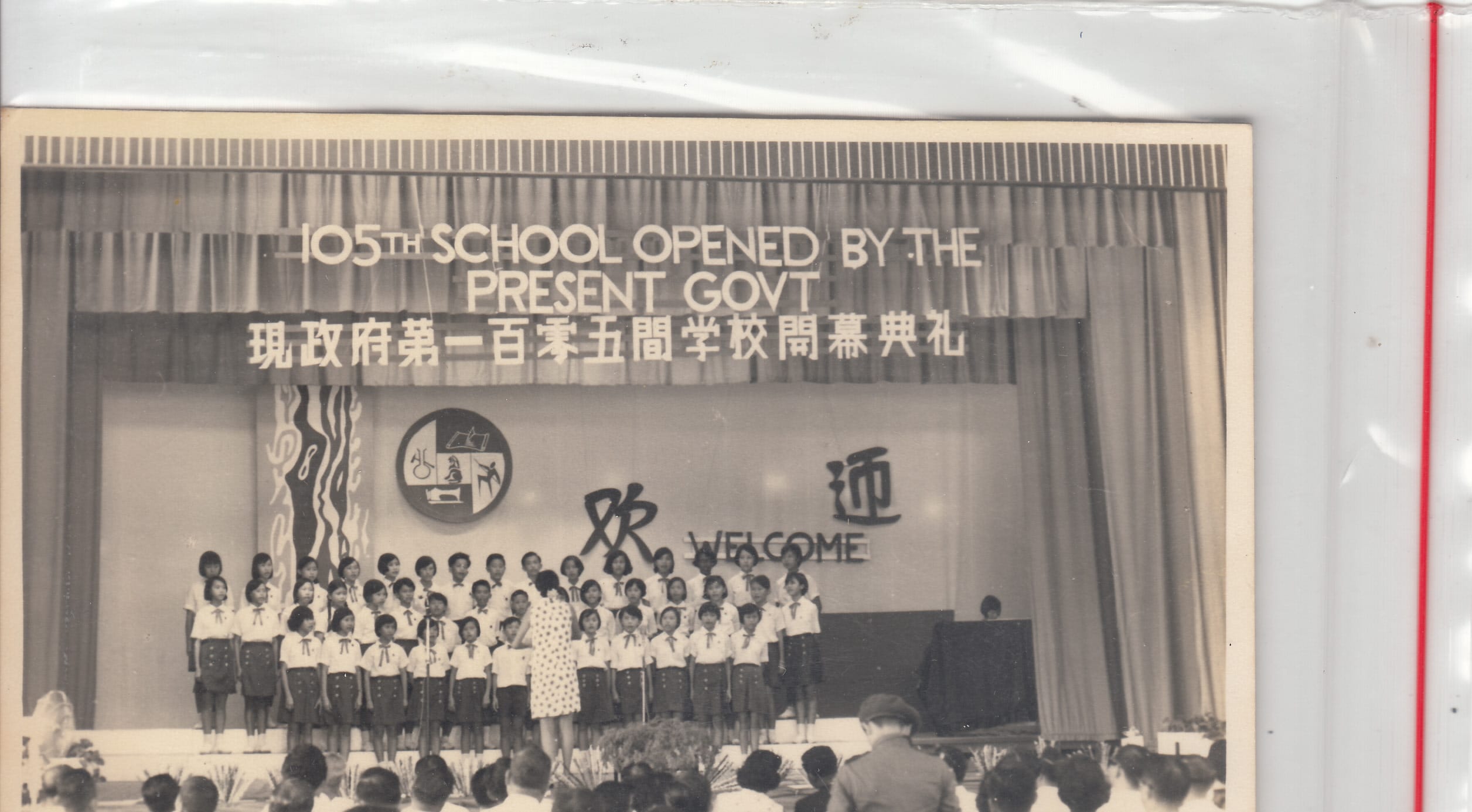 Children in uniform perform on stage at the 105th school opening ceremony, with a bilingual welcome banner behind them.